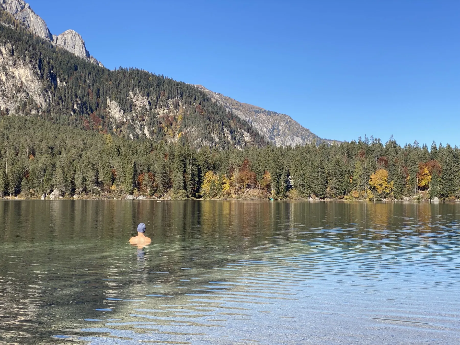 Una persona immersa fino alle spalle in un lago di montagna limpido, in autunno