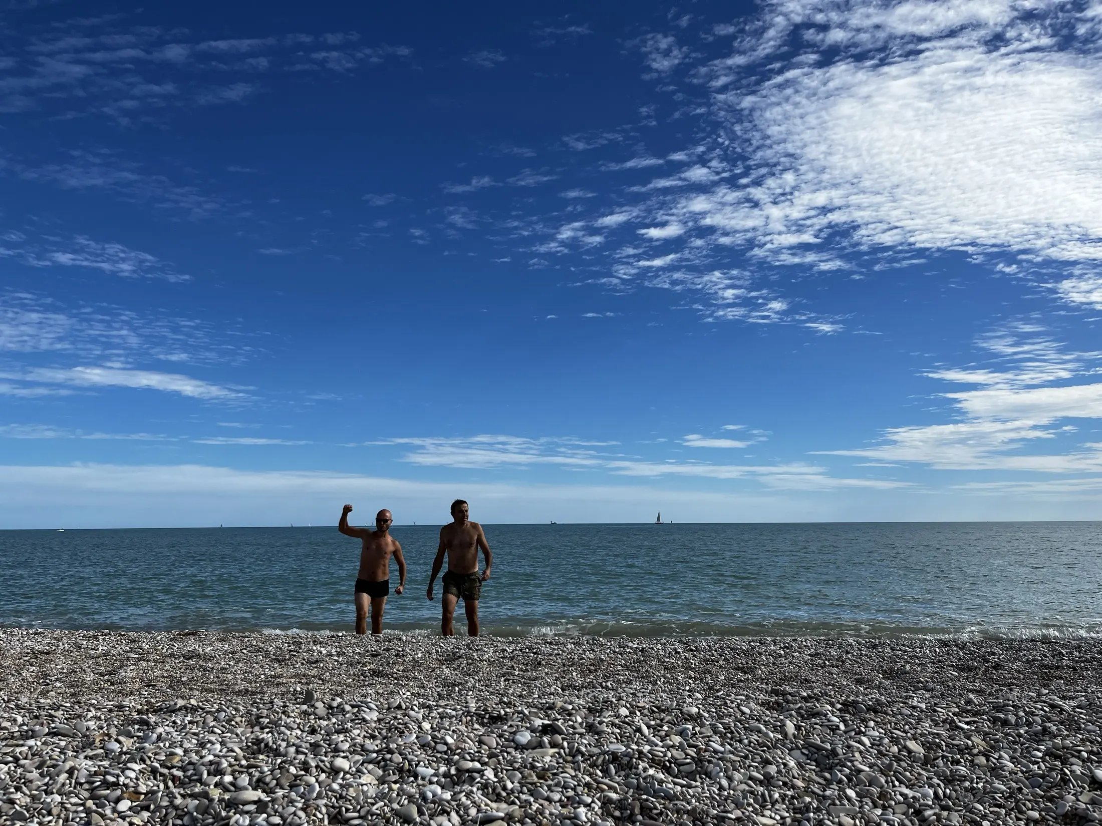 Due persone escono dal mare d'inverno su una spiaggia di sassi, una alza il braccio